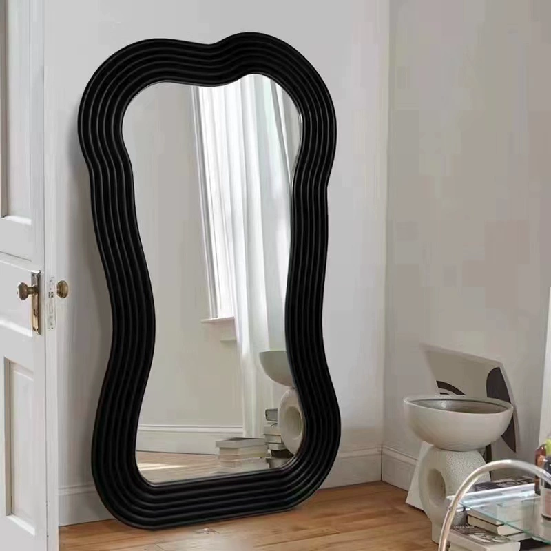 Full-length black mirror in a bright bedroom setting showcasing its unique shape.