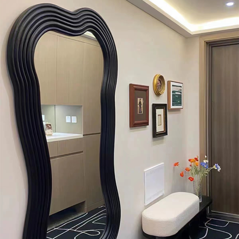 Full-length black mirror in a bright bedroom setting showcasing its unique shape.