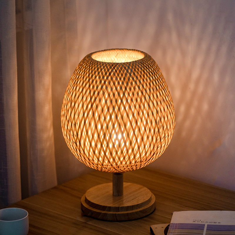 Front view of handwoven bamboo lamp with wooden base in a cozy bedroom setting.