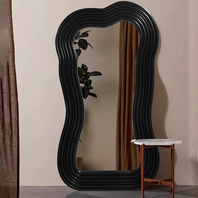 Full-length black mirror in a bright bedroom setting showcasing its unique shape.