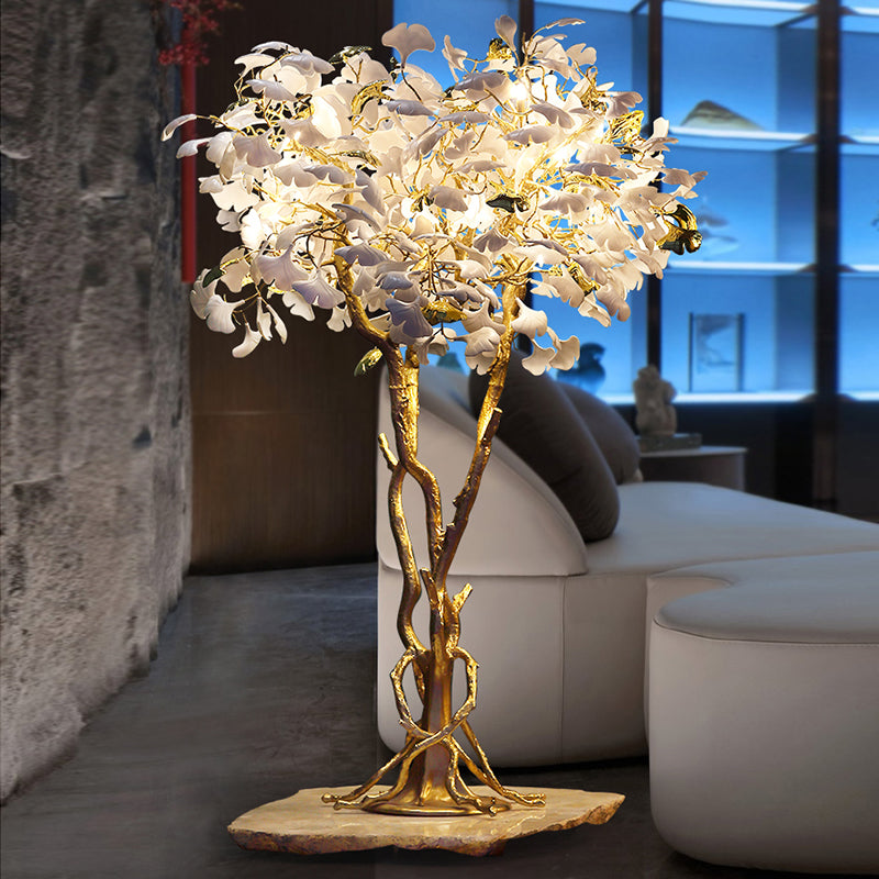 Ginkgo tree floor lamp glowing warmly in a stylish living room corner.