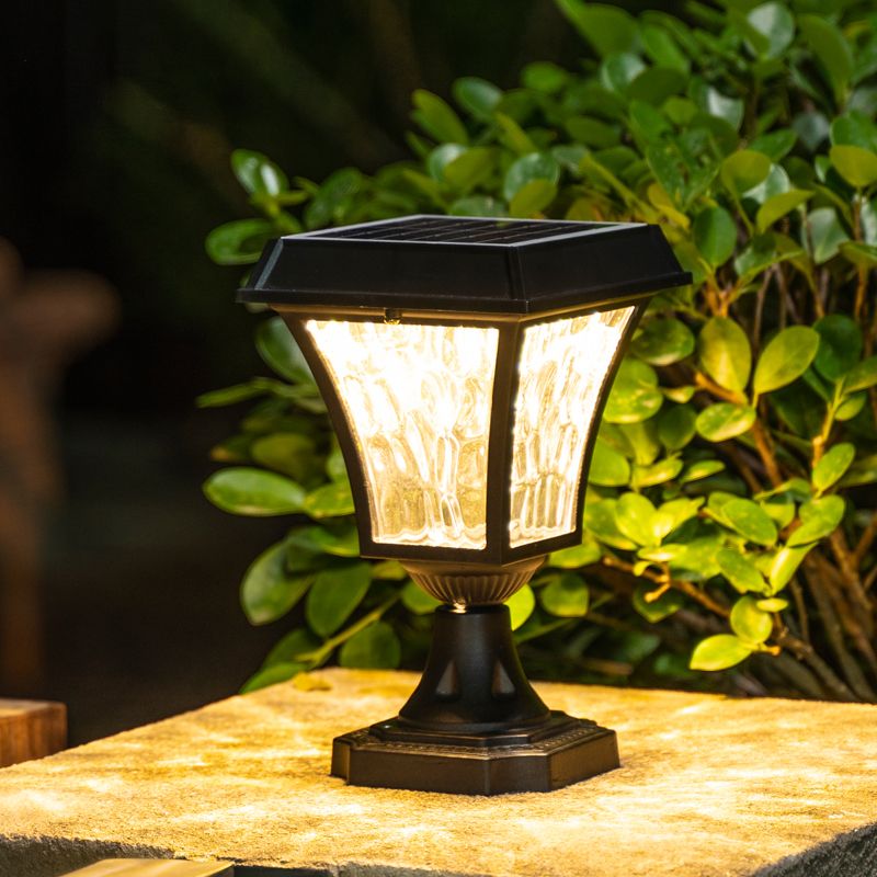 Black solar LED post light illuminating a courtyard at night.
