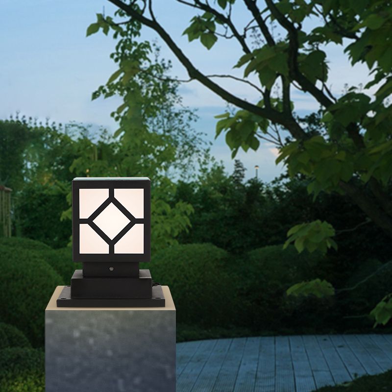 Black metal post lantern illuminating a driveway at dusk.