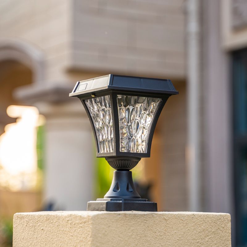 Black solar LED post light illuminating a courtyard at night.