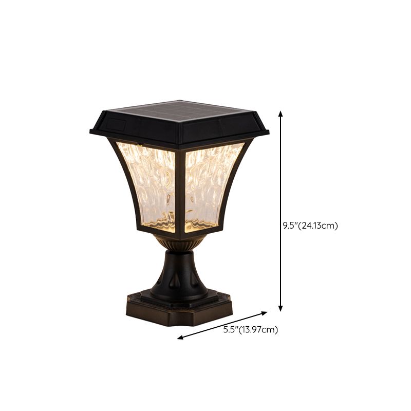Black solar LED post light illuminating a courtyard at night.