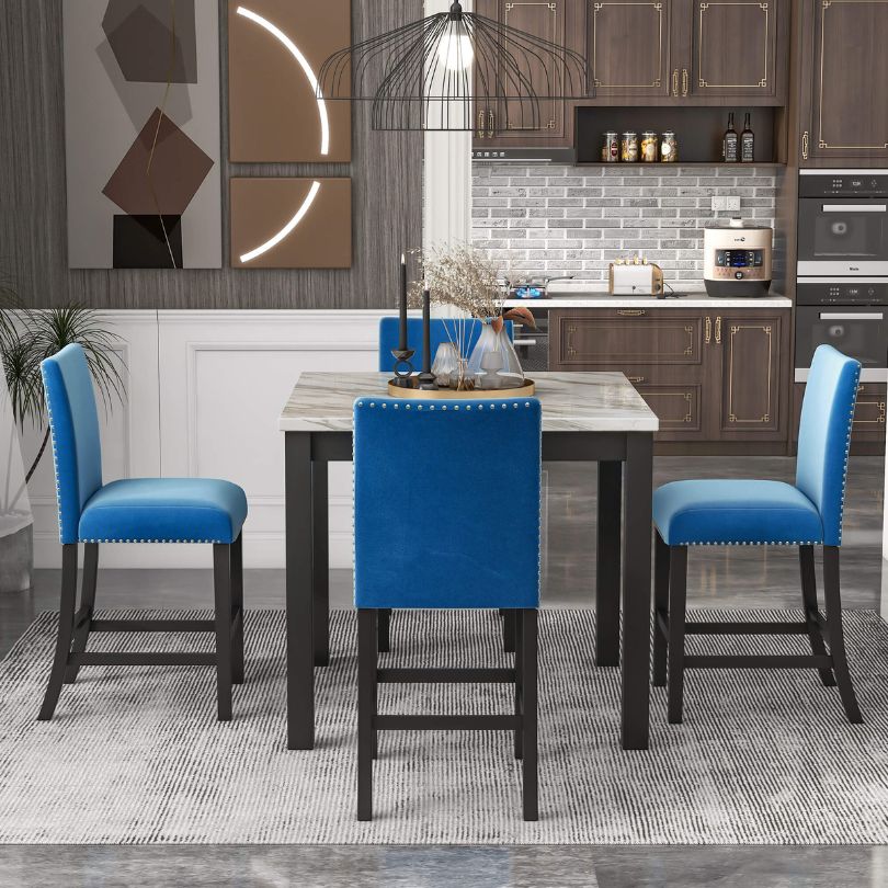 Elegant counter height dining table set showcasing four blue upholstered chairs and a faux marble table from the side view.