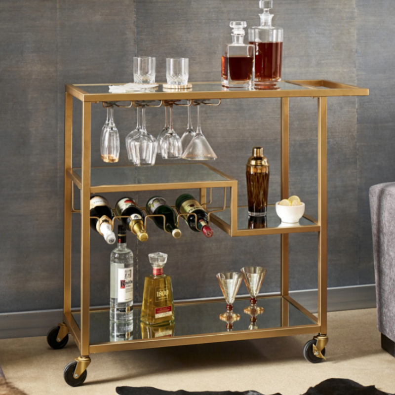 Four-wheeled champagne gold mirror cart positioned next to a cozy seating area.