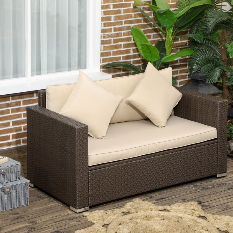 Beige outdoor wicker loveseat on a patio setting with throw pillows