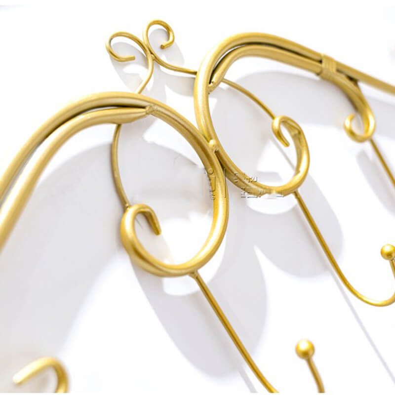 Angled view of the RetroWall™ metal coat rack in gold finish mounted on an entryway wall with coats hanging