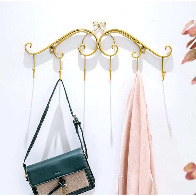 Angled view of the RetroWall™ metal coat rack in gold finish mounted on an entryway wall with coats hanging