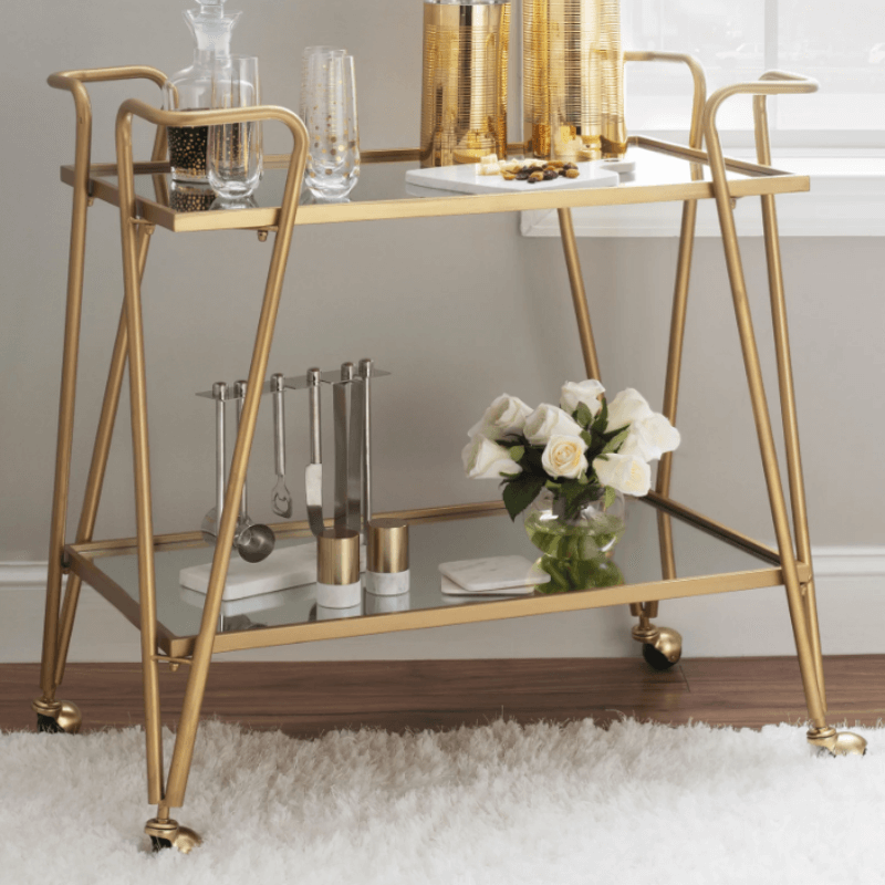 Modern mirrored bar cart with wheels positioned in a cozy living room setting.