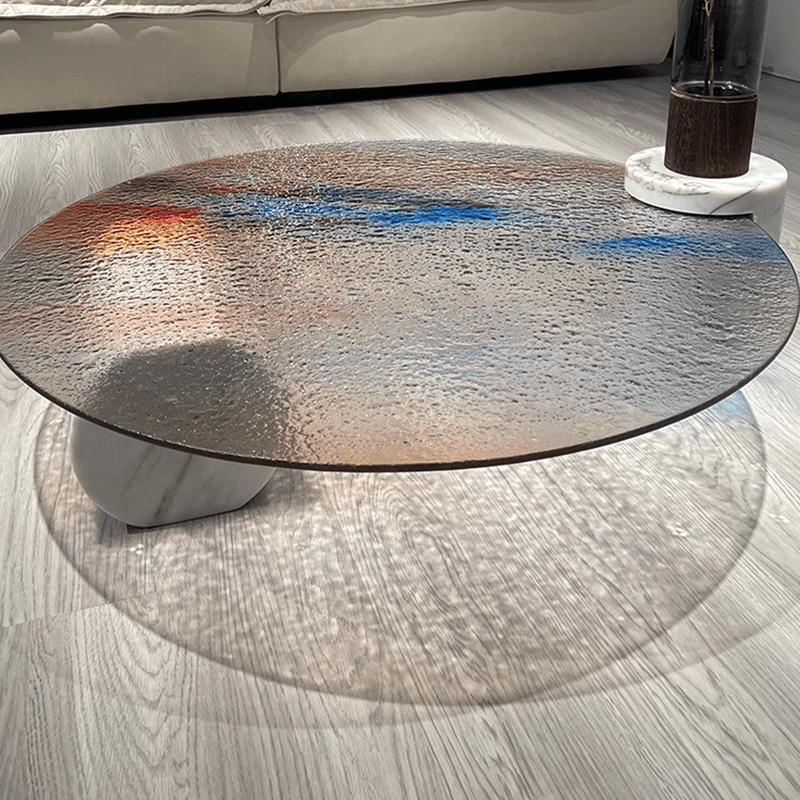 The ripple glass coffee table placed on a terrace, surrounded by lush plants and outdoor furniture.