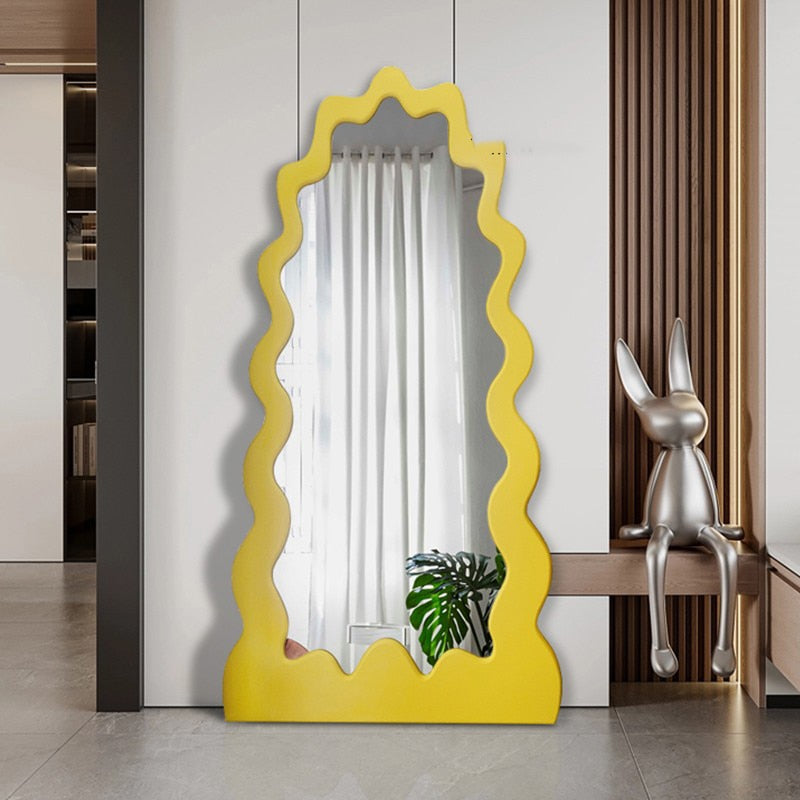 Full-length mirror with yellow wavy frame standing freely near a living room window