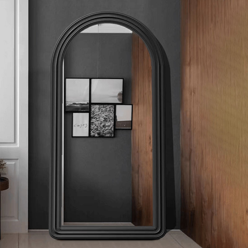 Black wall mirror with arched frame reflecting a chic bedroom atmosphere.