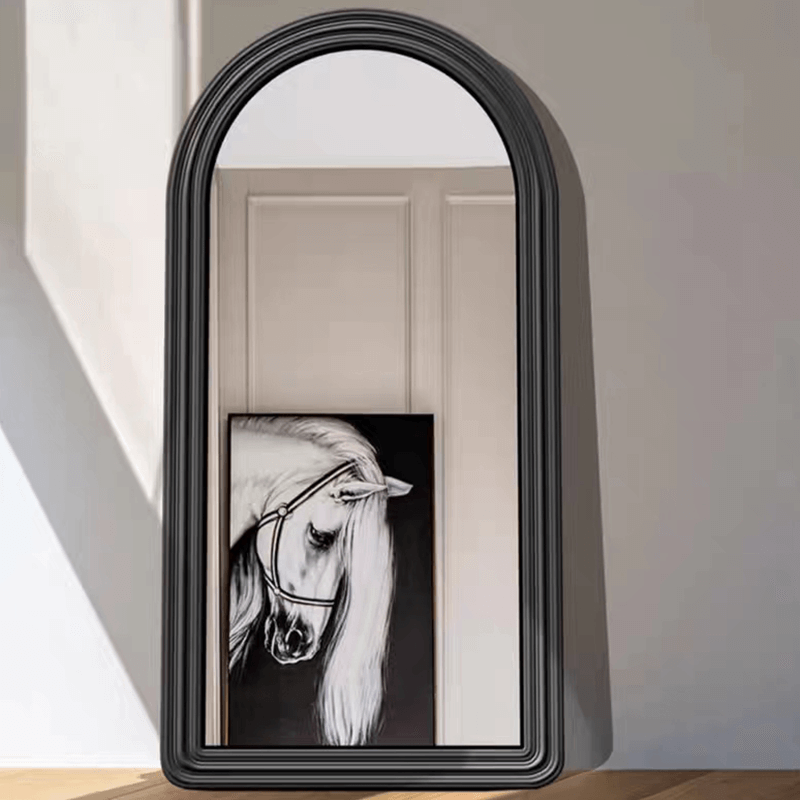 Black wall mirror with arched frame reflecting a chic bedroom atmosphere.