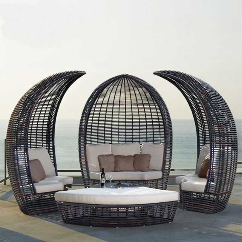 Elegant round rattan poolside daybed in a sunny garden setting, showcasing its sleek design and canopy.