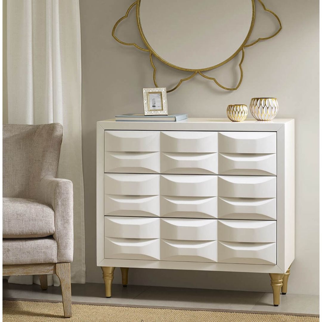 Angled front view of modern chest with white gloss finish and gold metal legs, showing all 3 drawers