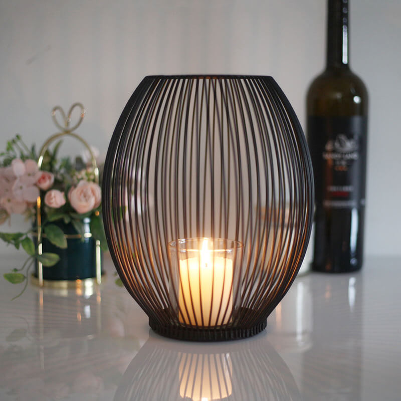 Large size iron candle holder on wooden coffee table with candlelight glowing through cage design.