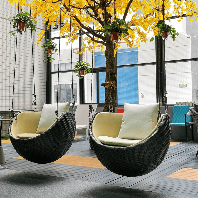 Side angle of the hanging rattan rocking chair in a garden, showing sturdy construction