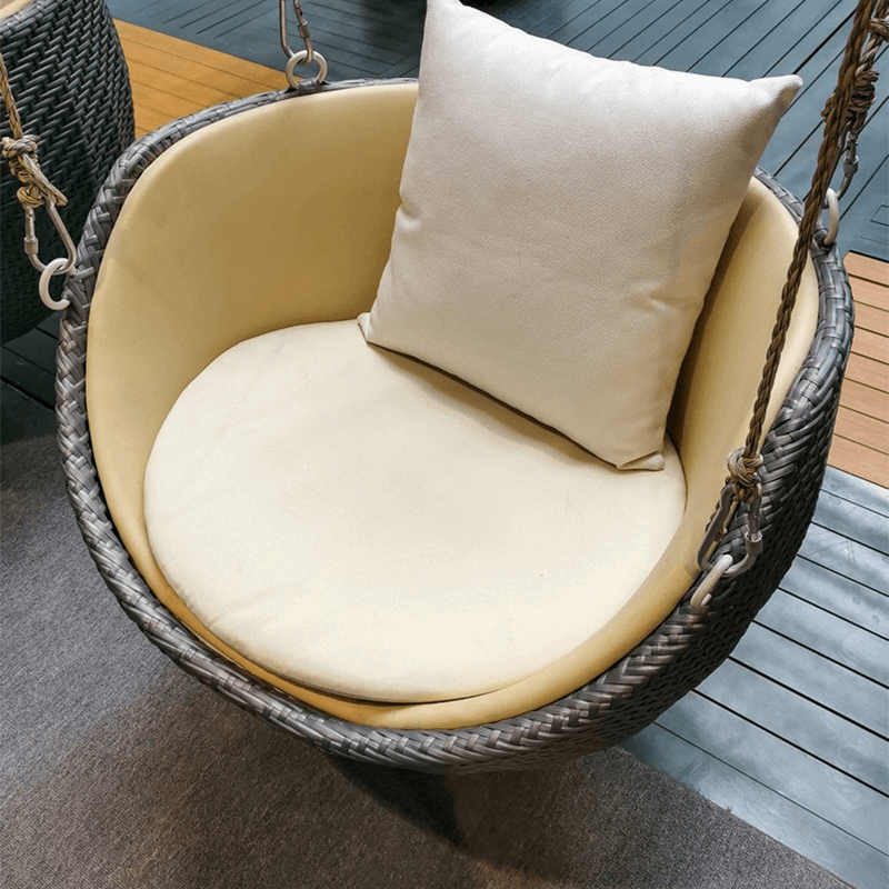 Close-up view of luxury rattan swing rocking chair on a patio with a cozy cushion