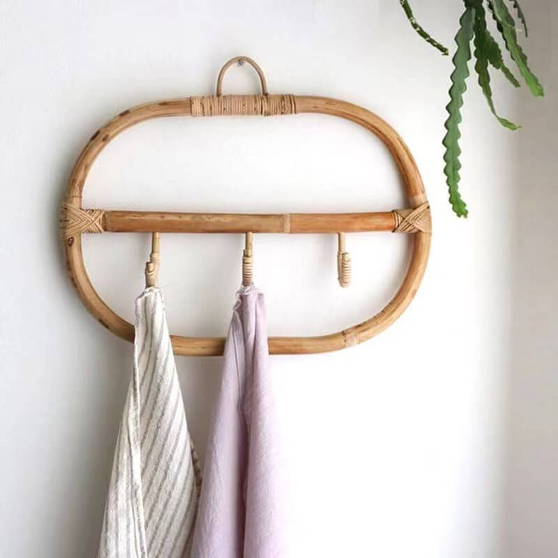 Elegant rattan coat hanger with three decorative hooks against a modern wall.