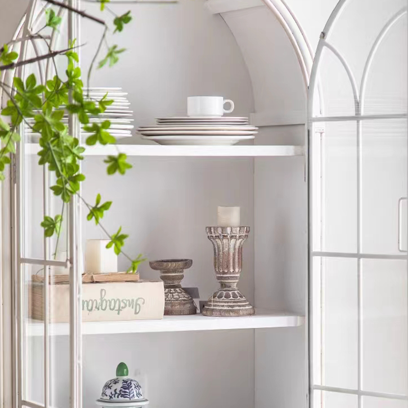 Front-facing image of white bookshelf with arched top and glass doors showcasing decor items